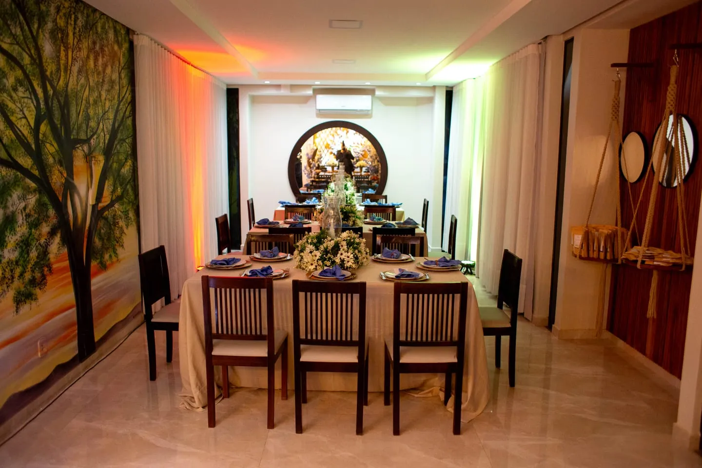 Salão montado para jantar, com a janela circular iluminada ao fundo