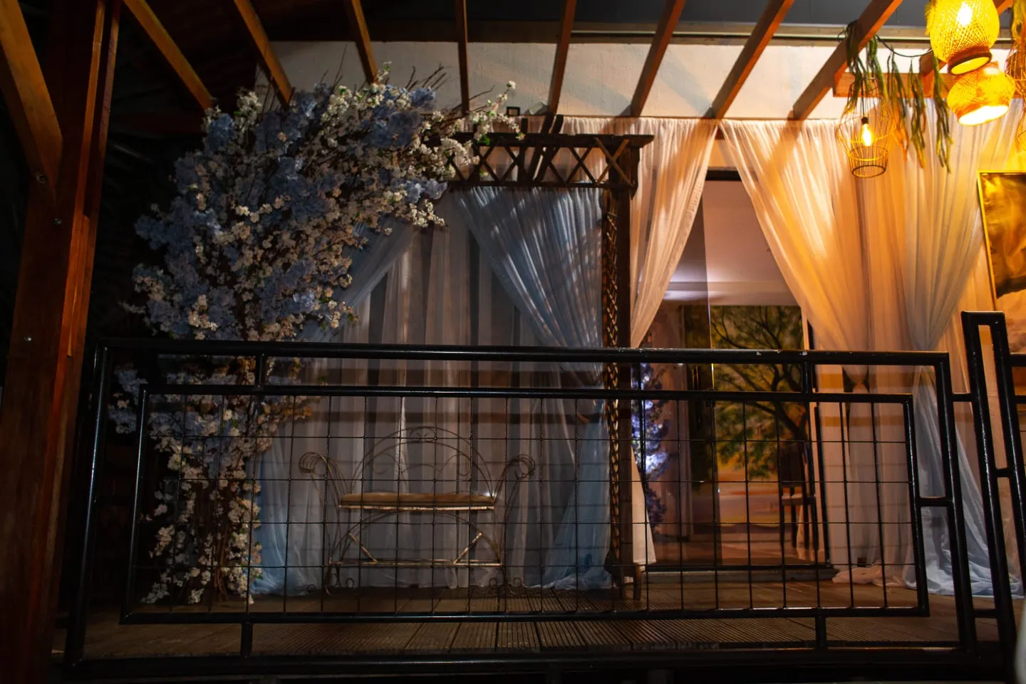 Varanda decorada com árvore florida, cortinas de voal e luminárias de palha